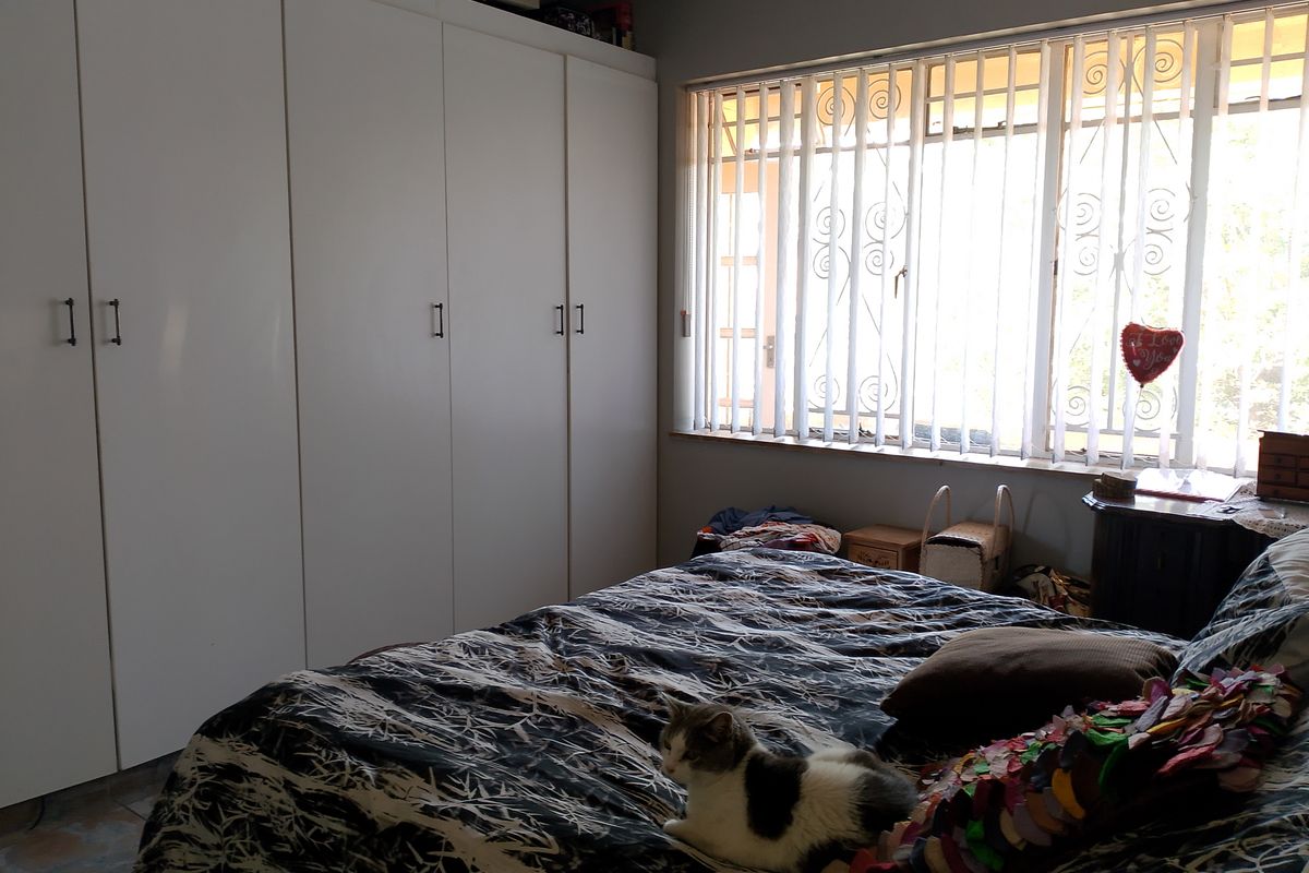 A bedroom featuring built-in floor-to-ceiling wardrobes and large windows with security bars, providing natural light.