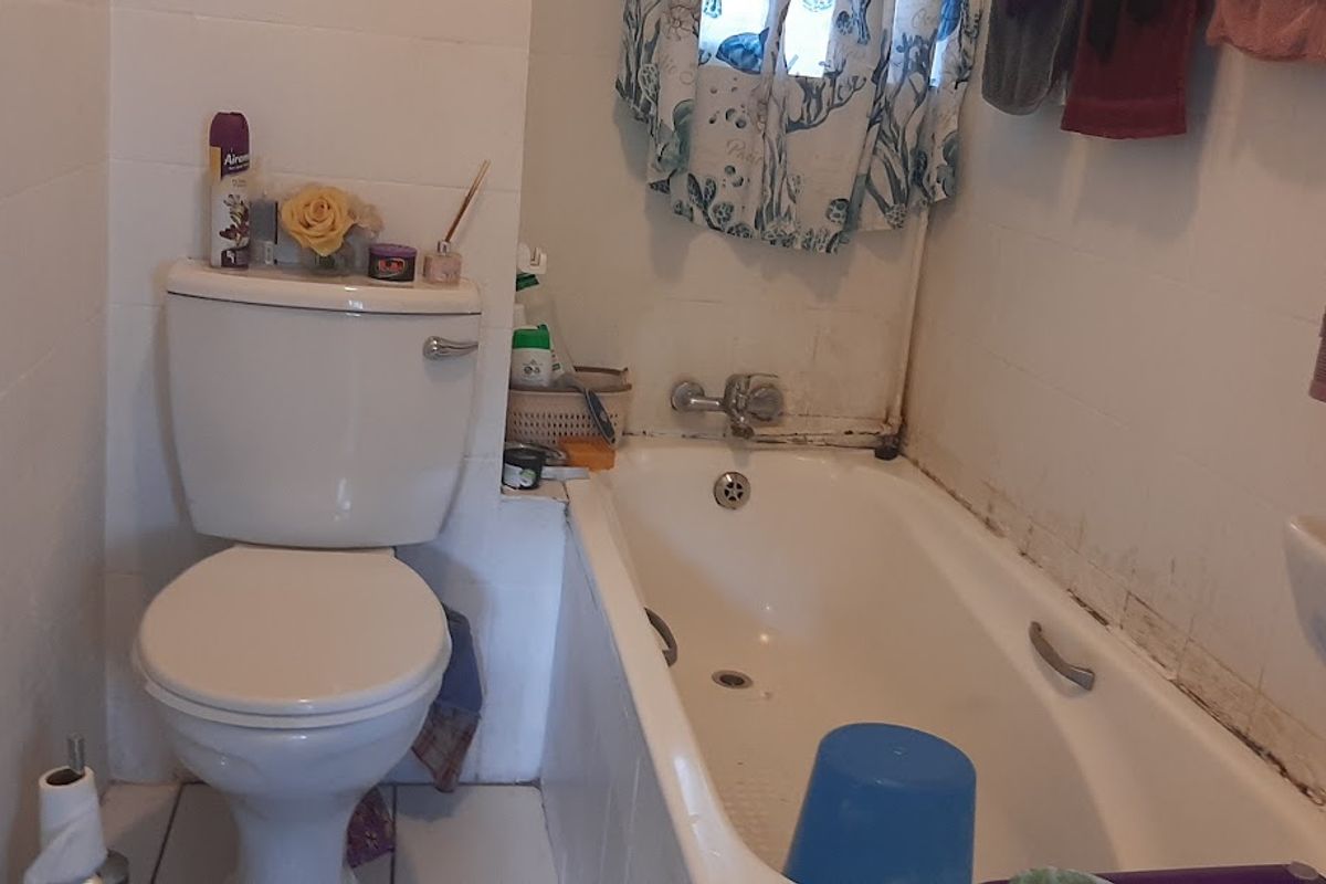 A compact bathroom featuring a standard bathtub, toilet, and basin with tiled finishes, requiring some maintenance and cosmetic updates.