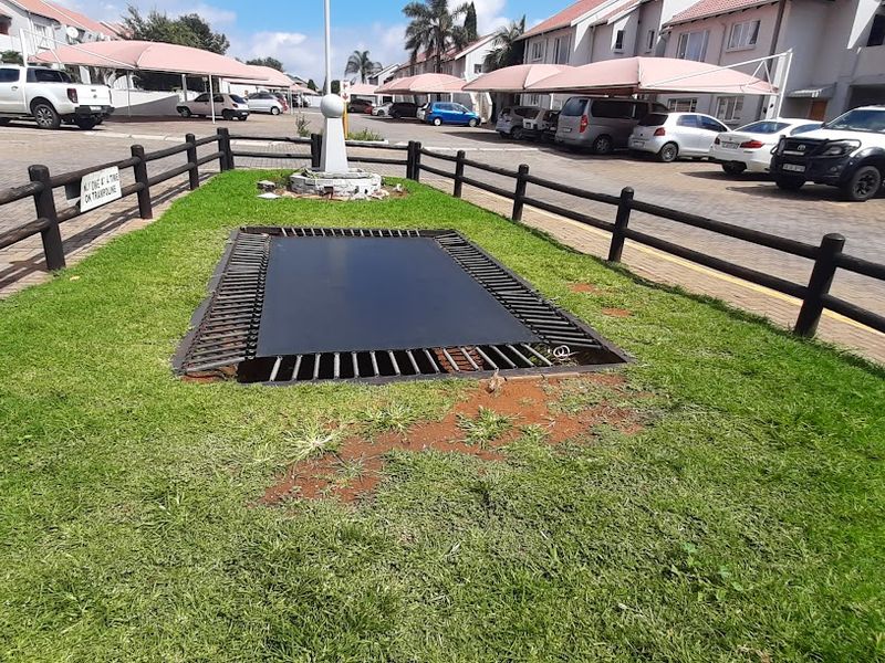 Communal garden area featuring an in-ground trampoline, enclosed by timber fencing, situated within a townhouse complex with paved parking and carports.