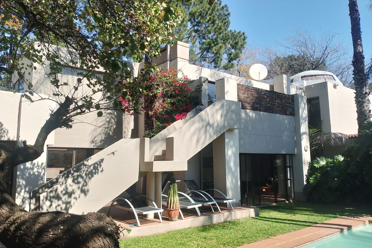 Rear elevation of a multi-level home featuring an external staircase, stone accent wall, sliding glass doors, and a swimming pool in the garden.