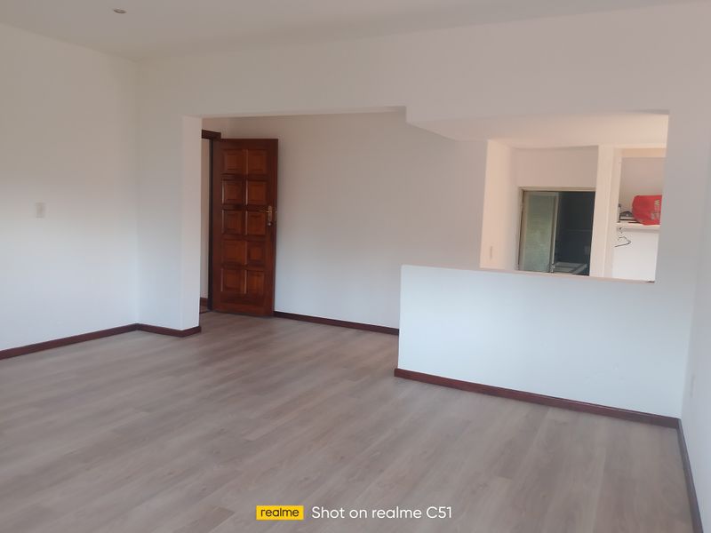 An empty open-plan living area featuring light-toned laminate flooring, neutral walls, and a solid timber entrance door.