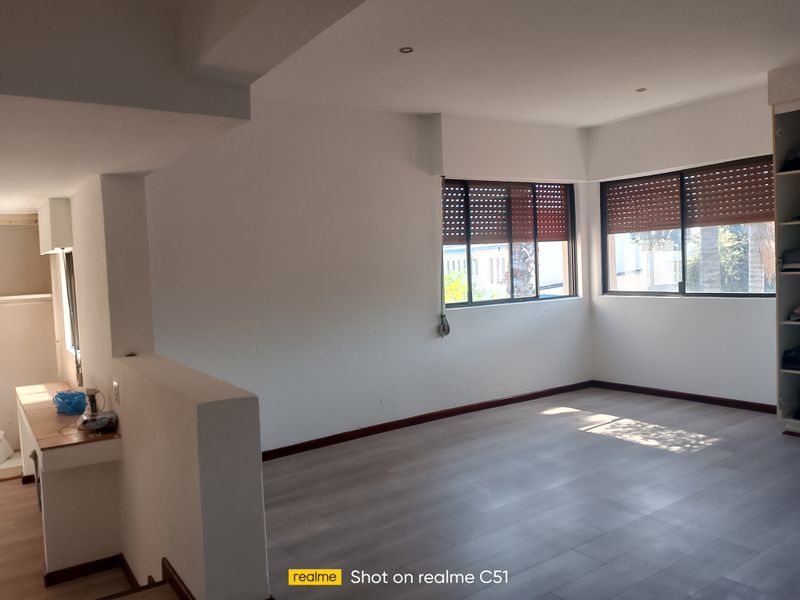 Spacious bedroom featuring light-toned laminate flooring, recessed ceiling lighting, and integrated built-in wardrobe storage with external security shutters on the windows.