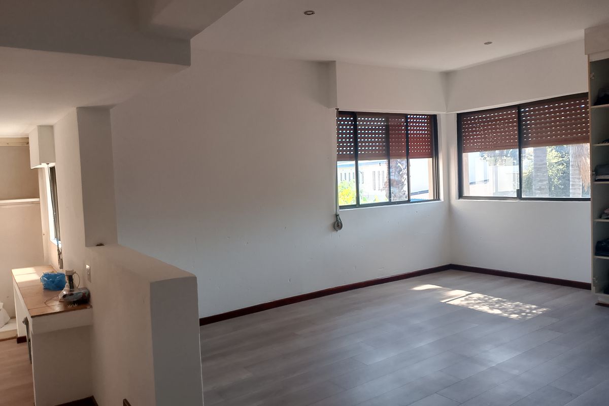 Spacious bedroom featuring light-toned laminate flooring, recessed ceiling lighting, and integrated built-in wardrobe storage with external security shutters on the windows.