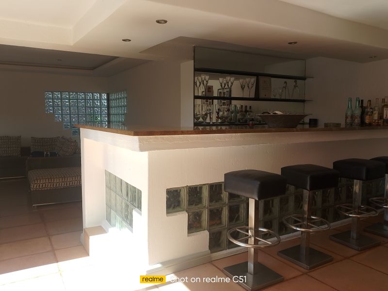 A dedicated bar area featuring a built-in counter with glass block detailing, mirrored shelving, and recessed ceiling lighting.