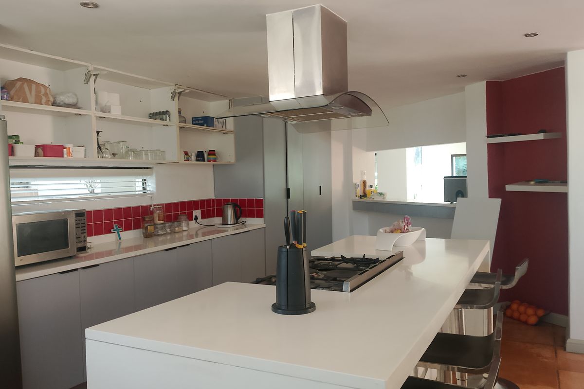 A kitchen featuring a central island with a gas cooktop, stainless steel extractor fan, and open shelving cabinetry with a red tiled backsplash.