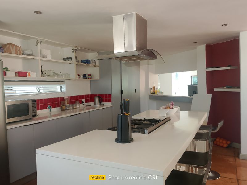 A kitchen featuring a central island with a gas cooktop, stainless steel extractor fan, and open shelving cabinetry with a red tiled backsplash.
