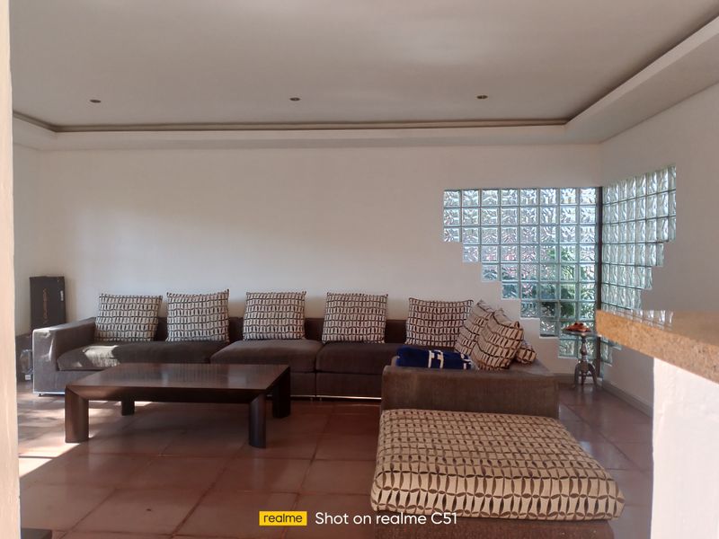 Spacious living room featuring a unique glass block feature wall, recessed ceiling lighting, and tiled flooring.