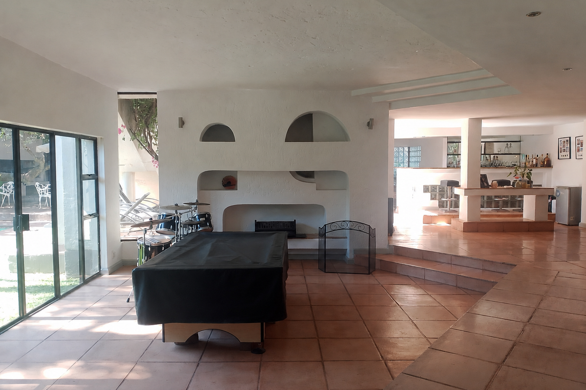 Spacious living area featuring a built-in fireplace, terracotta flooring, and a sunken bar area with direct access to the outdoor patio.