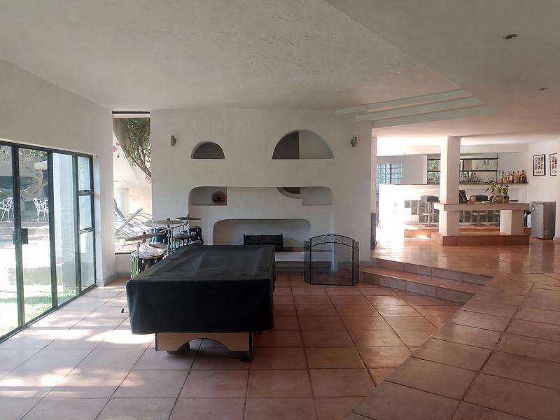 Spacious living area featuring a built-in fireplace, terracotta flooring, and a sunken bar area with direct access to the outdoor patio.