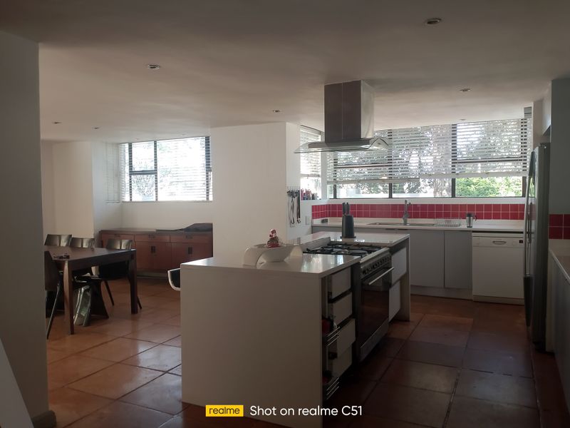 Open-plan kitchen and dining area featuring a central island with gas hob, tiled flooring, and red backsplash, offering a functional layout for modern living.