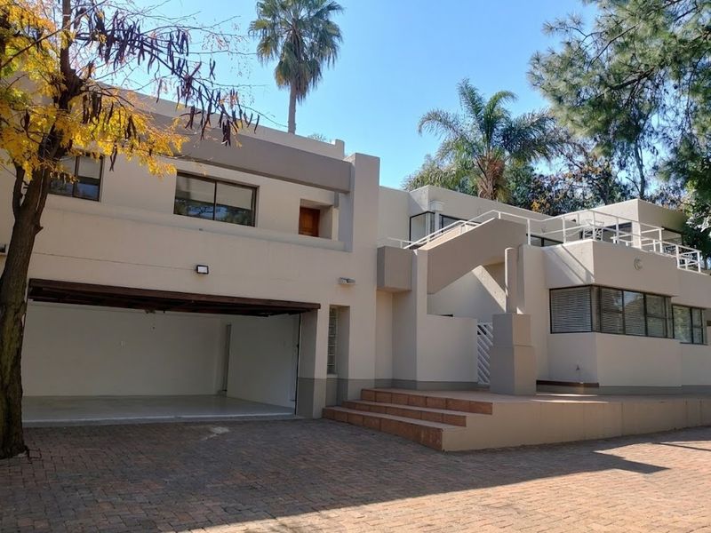 Front elevation of a modern multi-level house featuring a double garage, paved driveway, and an external staircase leading to an upper-level balcony.
