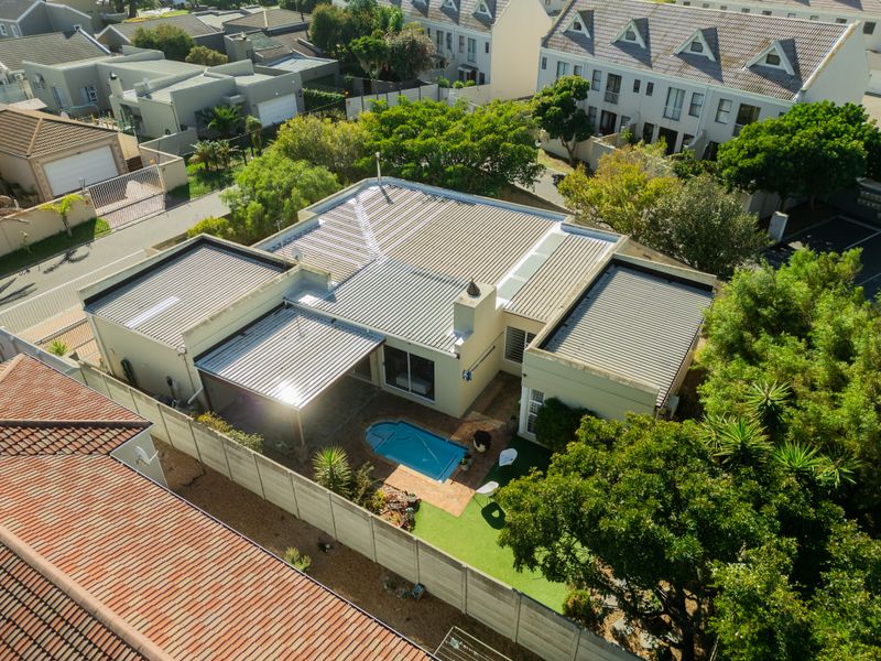 Aerial view of a residential property featuring a corrugated metal roof, a private swimming pool, a covered patio area, and a landscaped garden.