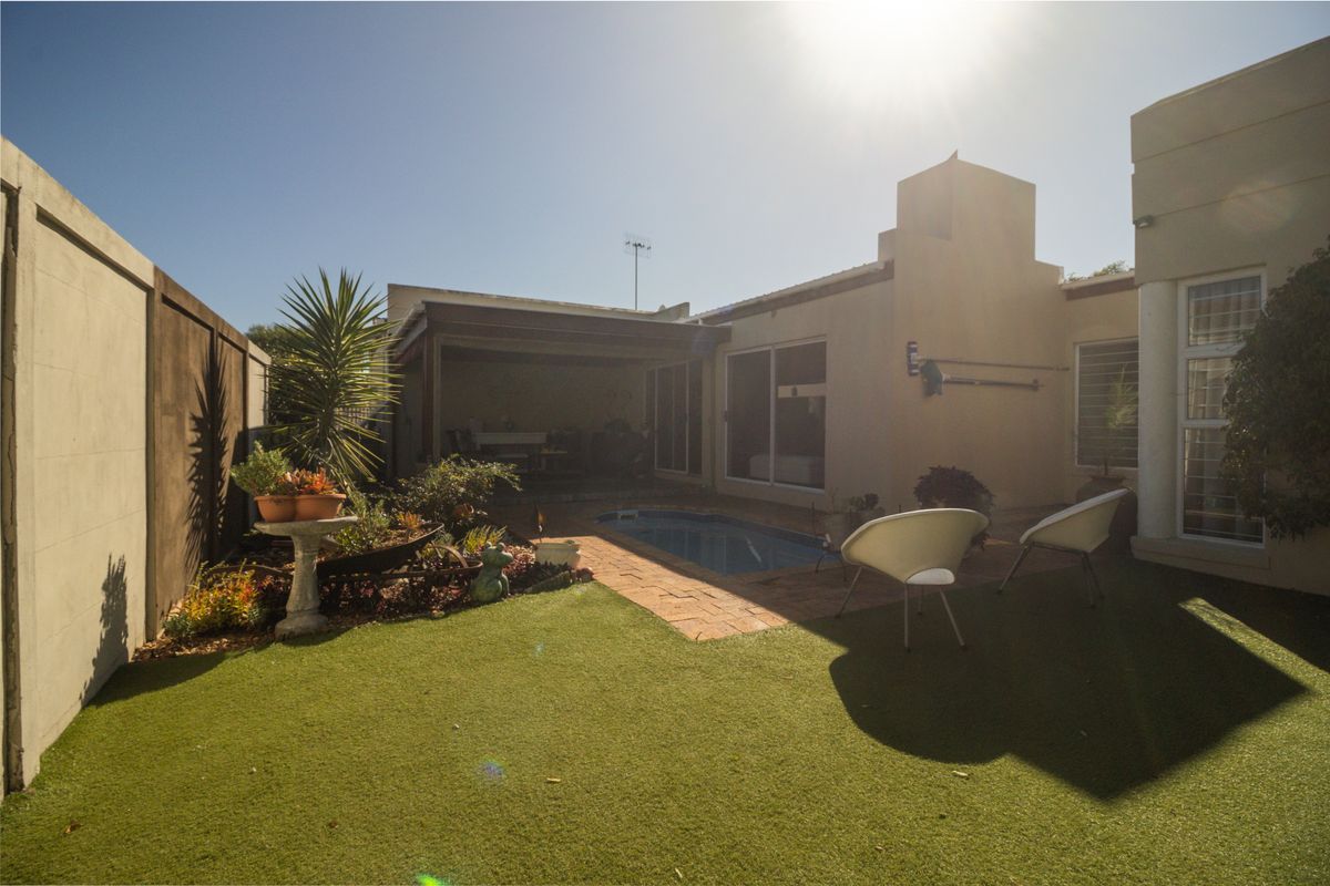 Rear exterior view featuring a compact swimming pool, covered patio area, artificial lawn, and brick paving, set against a private boundary wall.