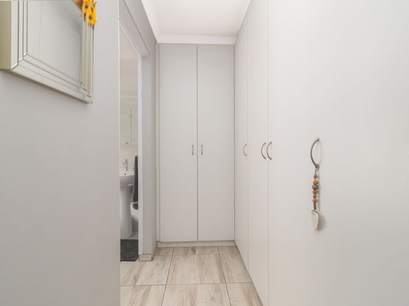 A clean, modern hallway featuring extensive built-in storage cupboards and light-toned tiled flooring, leading towards an adjacent bathroom.