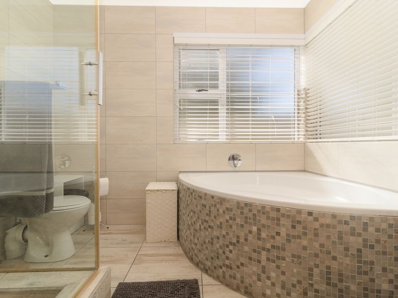 A well-maintained bathroom featuring a corner bathtub with mosaic tile detailing, a separate glass-enclosed shower, and neutral floor-to-ceiling wall tiles.