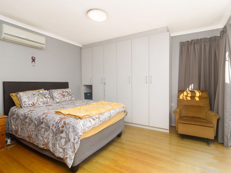 A well-maintained bedroom featuring laminate flooring, built-in cupboards, and a split-system air conditioner, with direct access to an outdoor area via a security gate.