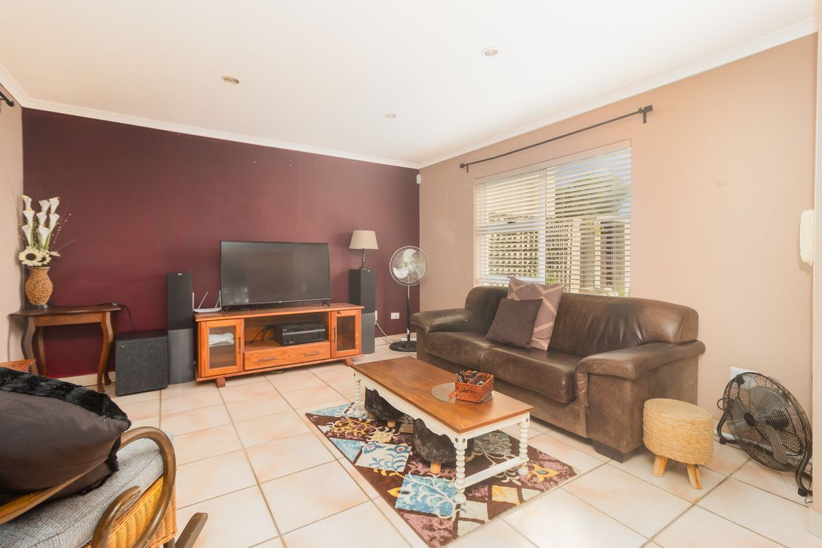 A living room featuring tiled flooring, recessed downlights, and venetian blinds, with a neutral and accent wall color scheme.