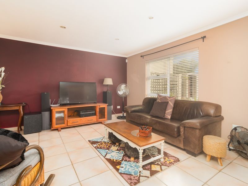 A living room featuring tiled flooring, recessed downlights, and venetian blinds, with a neutral and accent wall color scheme.