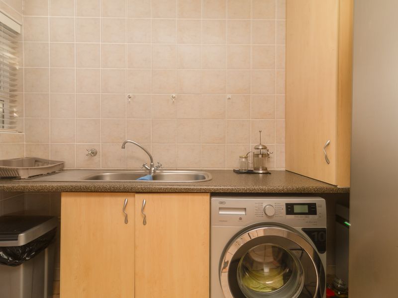 Functional laundry area featuring laminate cabinetry, a stainless steel sink, tiled backsplash, and space for a washing machine.