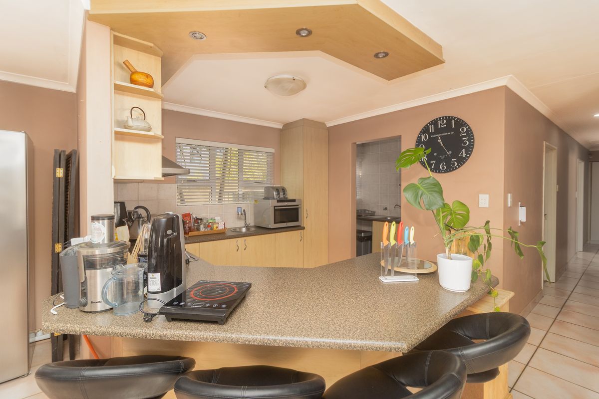 A functional kitchen featuring laminate cabinetry, a breakfast bar, and tiled flooring, with an adjacent scullery area visible in the background.