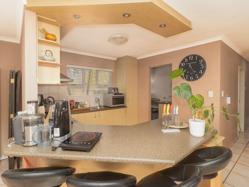 A functional kitchen featuring laminate cabinetry, a breakfast bar, and tiled flooring, with an adjacent scullery area visible in the background.