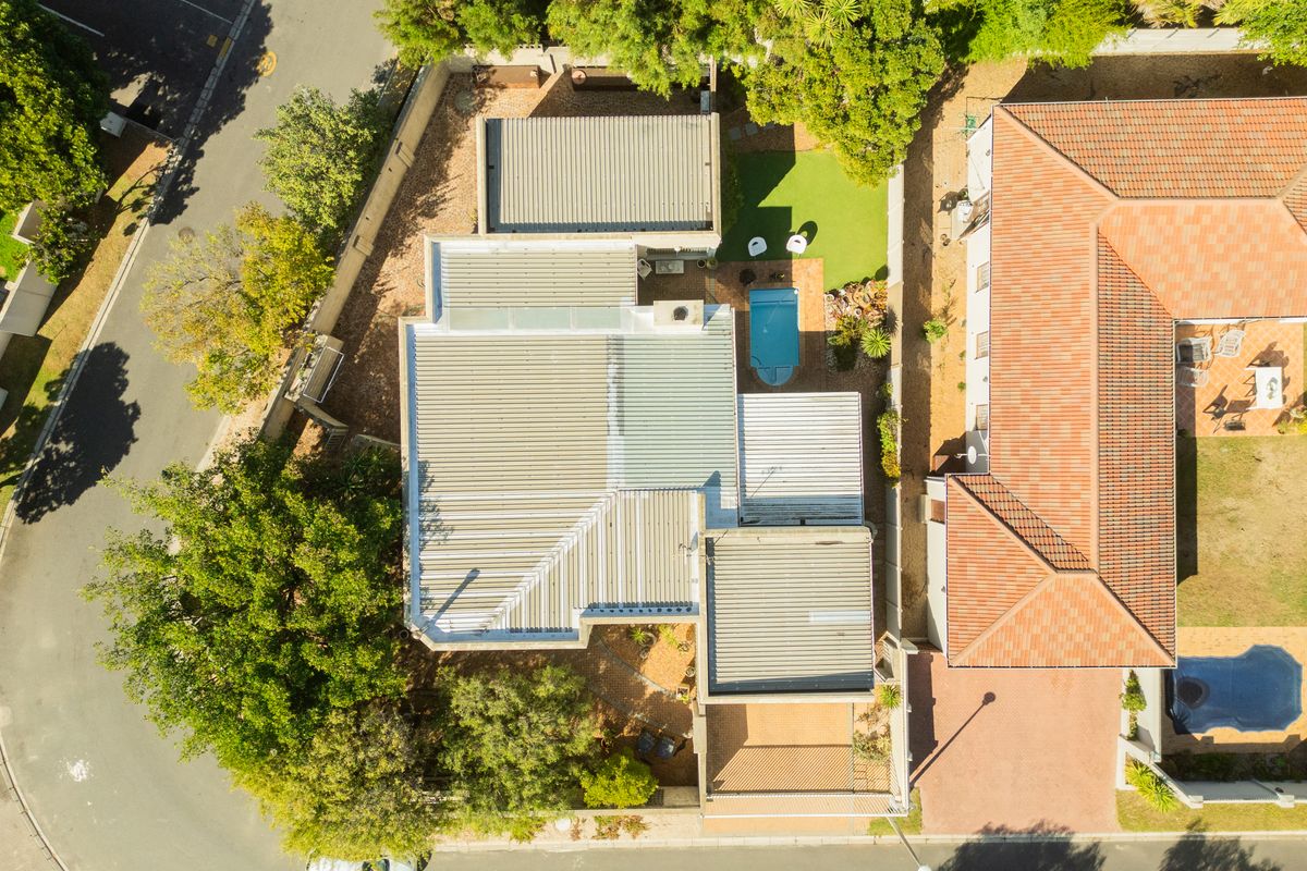 Aerial view of the property showing the roof structure, swimming pool, landscaped garden areas, and paved driveway access from the street.