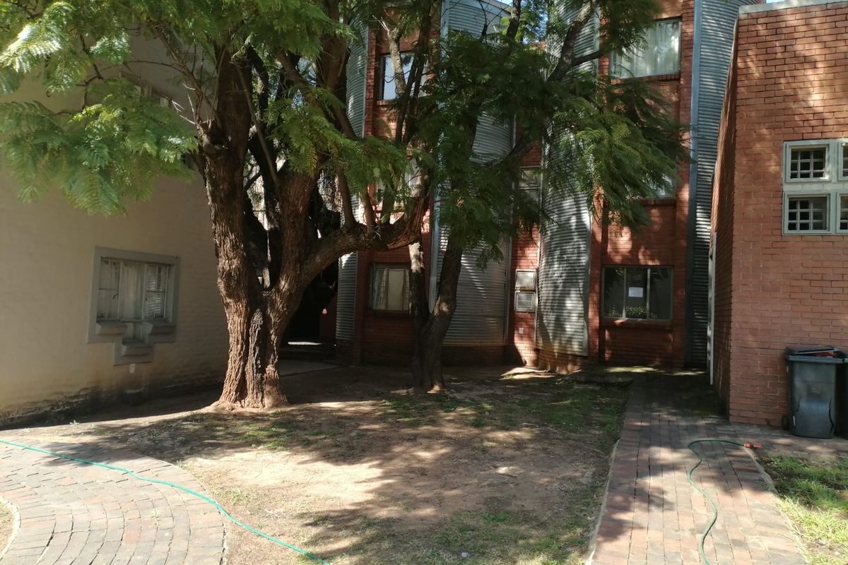 A view of the rear exterior of the townhouse, featuring brick and corrugated metal facade elements, mature trees, and a paved walkway.