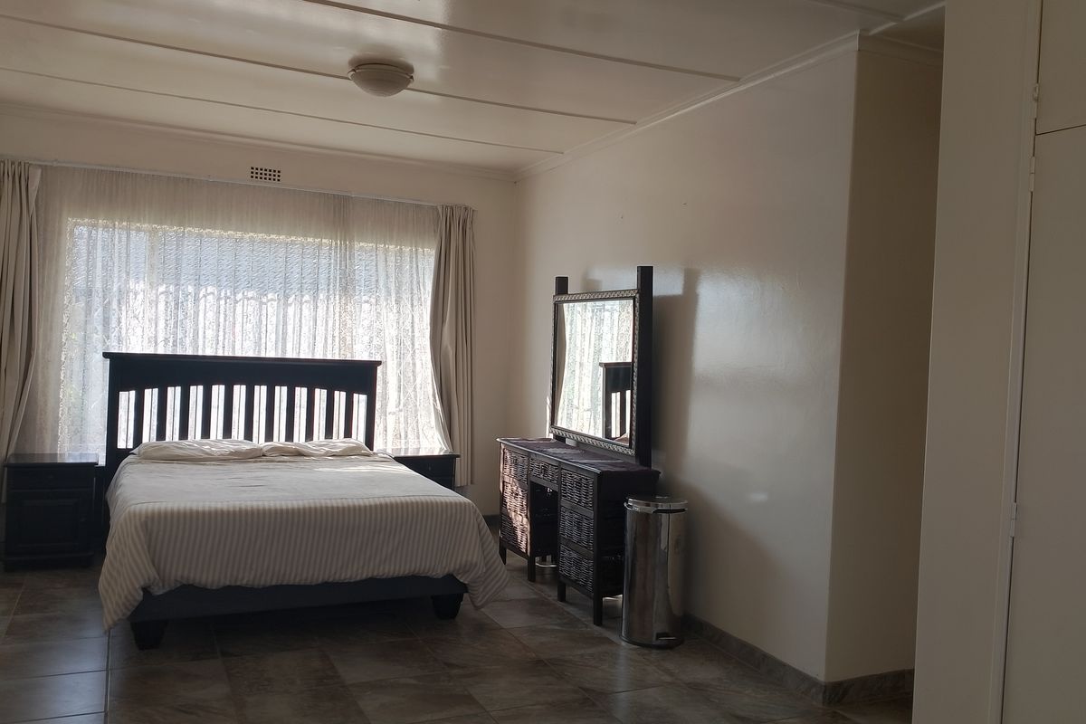 A spacious bedroom featuring tiled flooring, built-in cupboards, and large windows that allow for ample natural light.