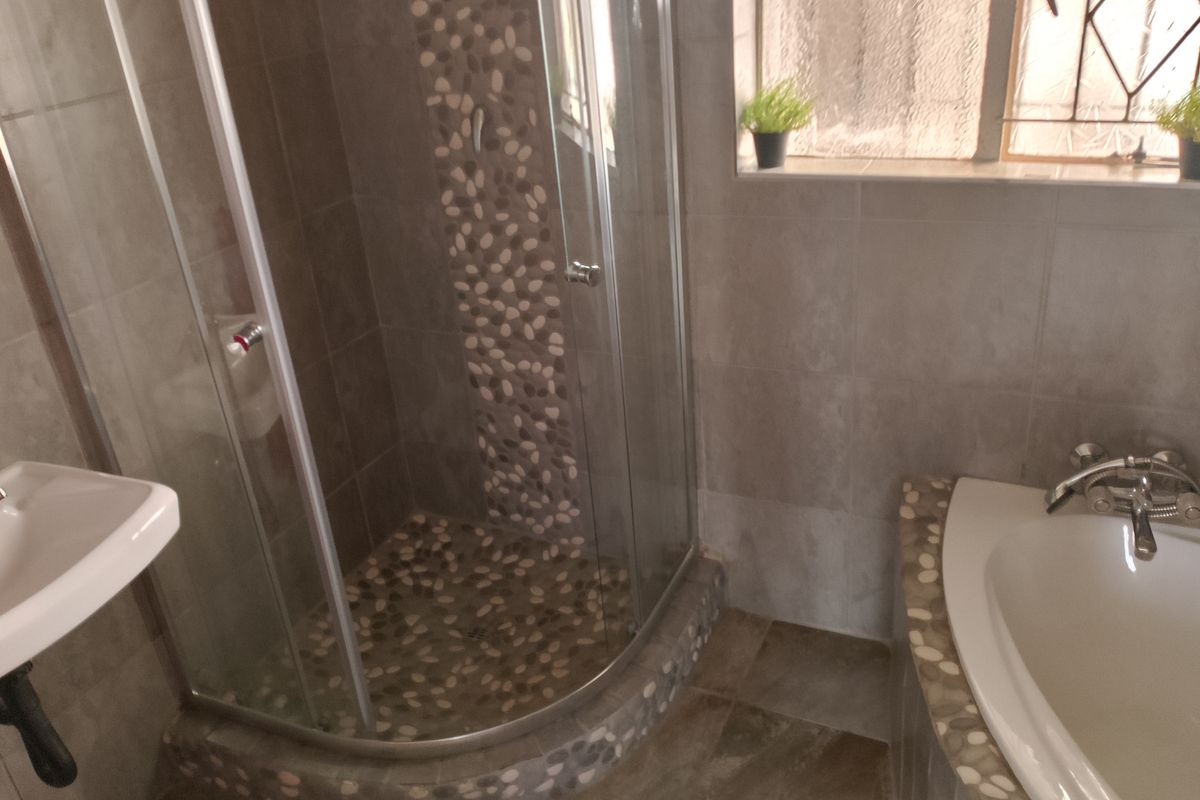 A modern bathroom featuring a corner shower enclosure with pebble-tiled accents, a built-in bathtub, and neutral wall tiling.