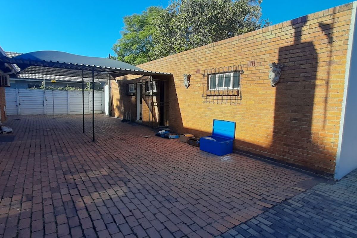 A paved rear courtyard area featuring a covered carport structure and exposed brick exterior walls with security bars on windows.