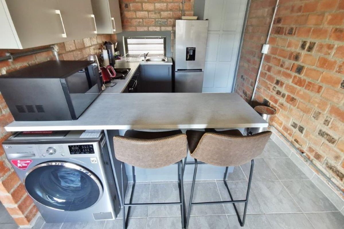 Compact kitchen featuring exposed brick walls, modern cabinetry, a breakfast bar, and integrated laundry space with tiled flooring.