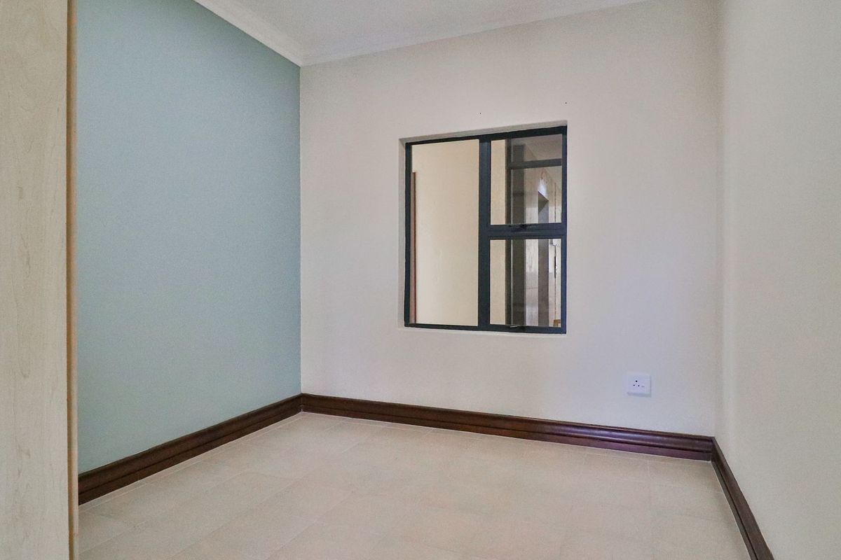 An empty bedroom featuring tiled flooring, a built-in cupboard, and a feature wall with an aluminium-framed window.