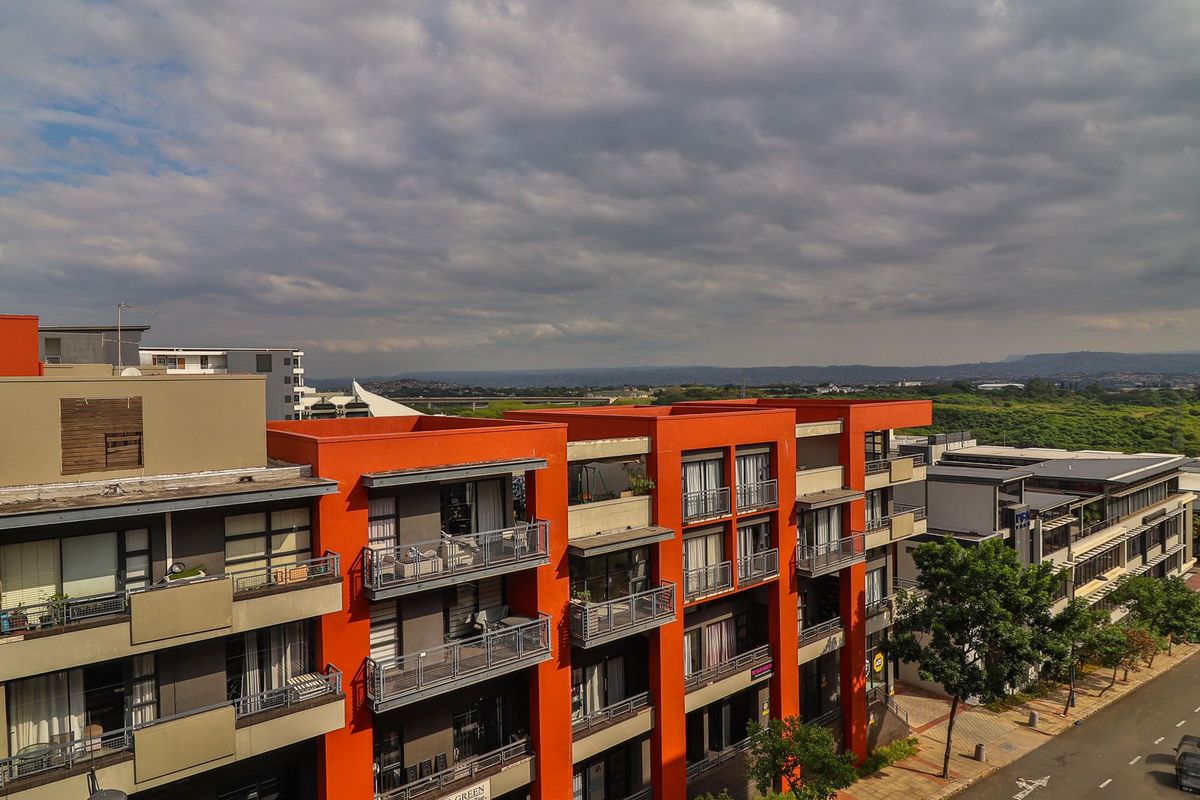 Aerial view of a modern apartment complex featuring orange facade accents, private balconies with metal railings, and surrounding street infrastructure.