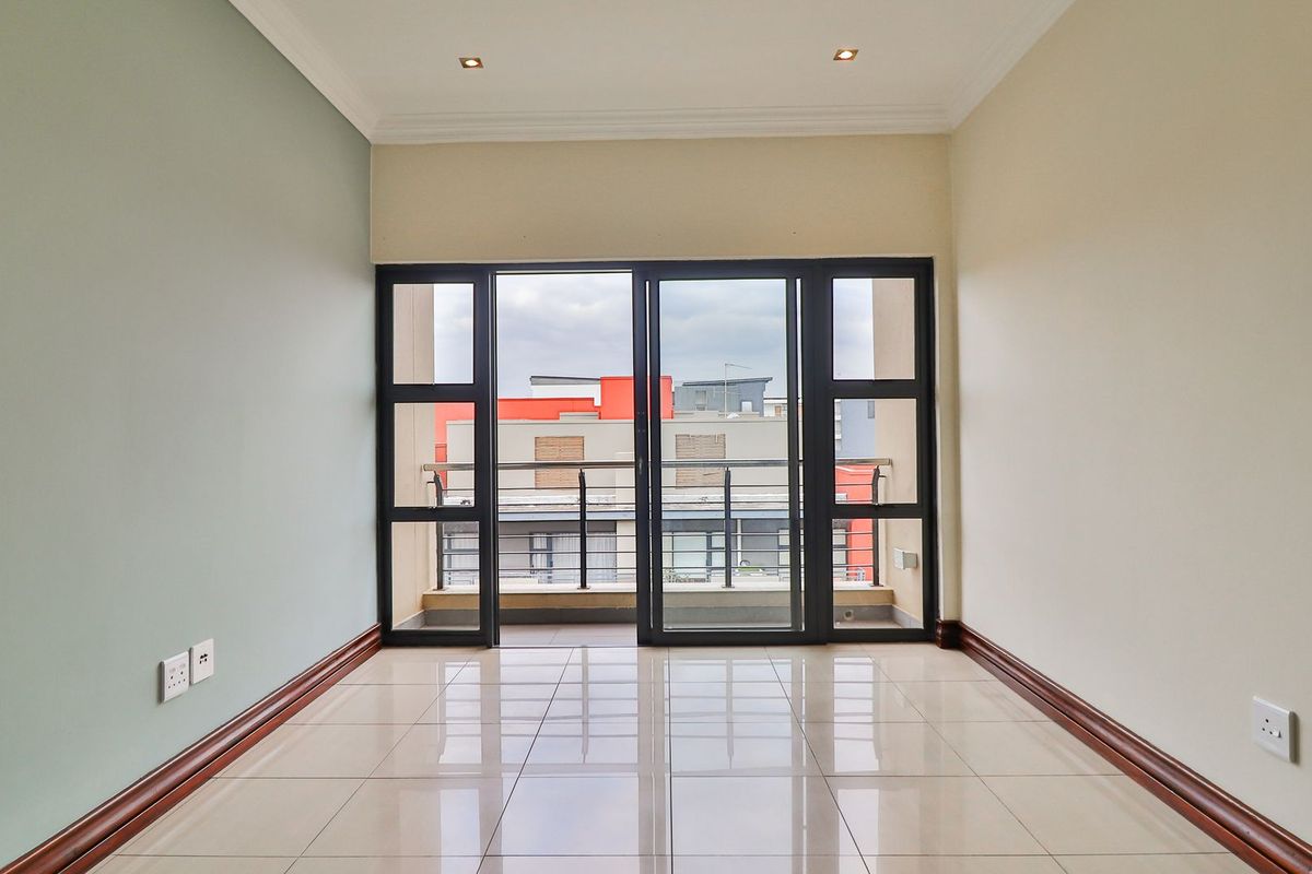 A bright, empty living room featuring neutral walls, tiled flooring, and large sliding glass doors that open onto a private balcony.