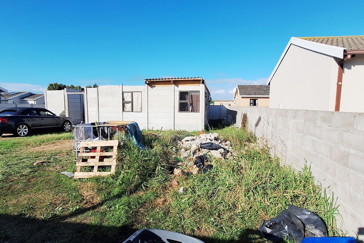 A vacant residential plot featuring a precast concrete structure, perimeter walling, and significant overgrown vegetation requiring clearing and site preparation.
