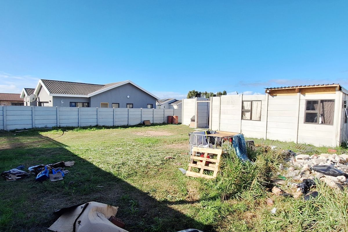 A vacant residential plot featuring perimeter precast concrete walling and a small, basic outbuilding structure in need of maintenance and clearing.
