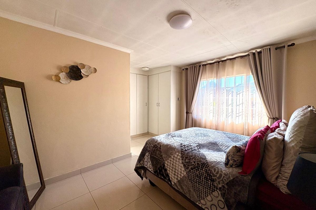 A well-lit bedroom featuring tiled flooring, built-in cupboards, and large windows with curtains, providing a functional and comfortable living space.