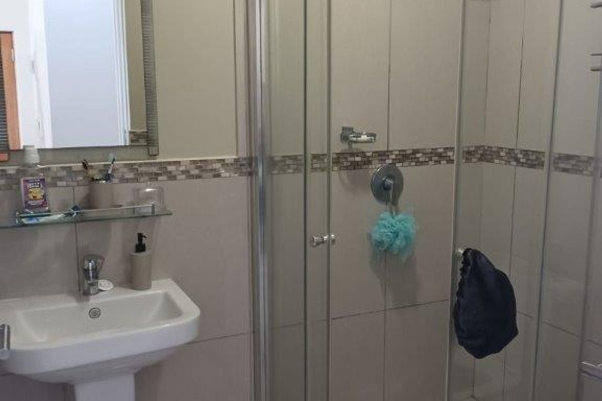 A functional bathroom featuring a glass-enclosed shower, a pedestal basin, and neutral wall tiling with a decorative mosaic border.
