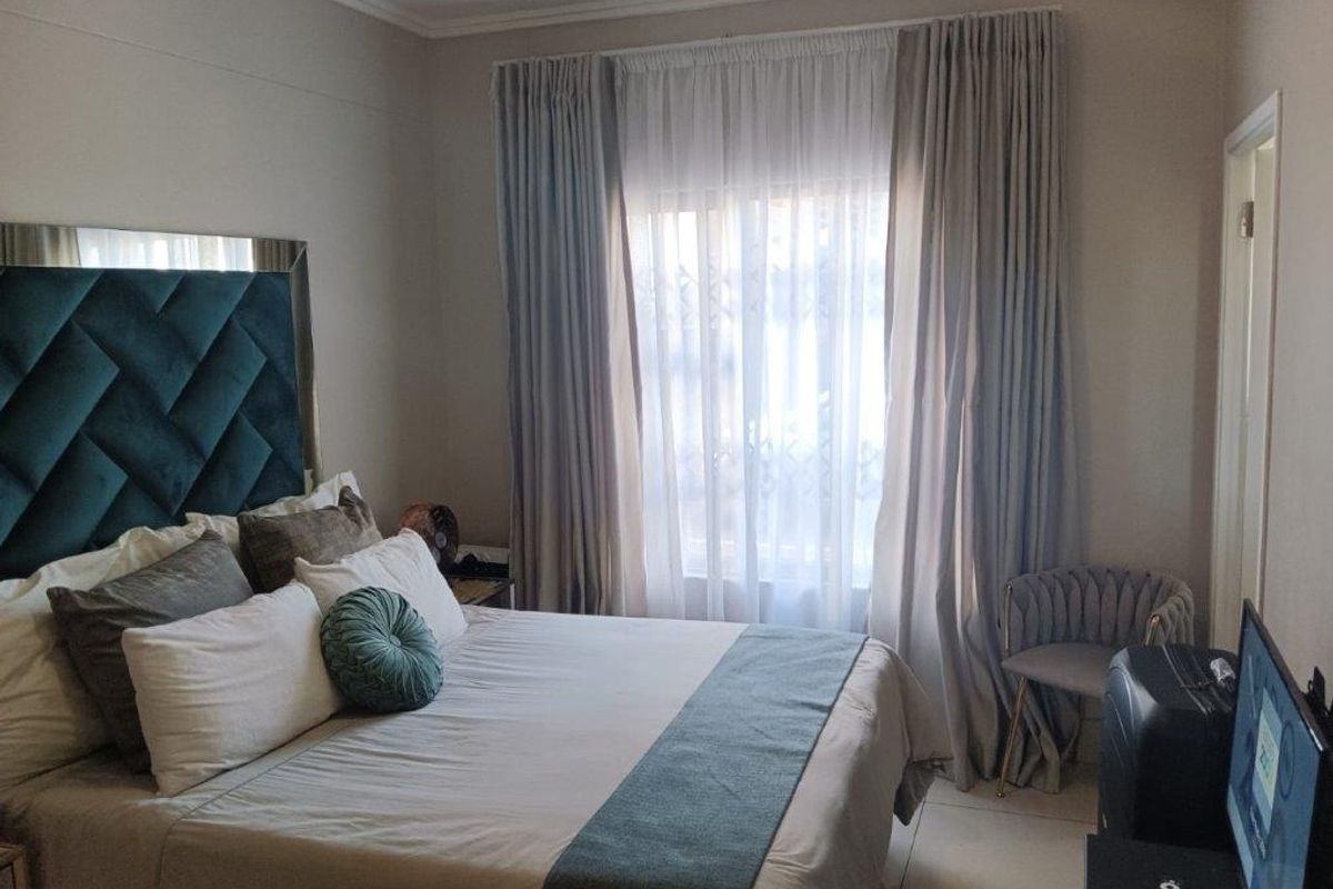 A well-maintained bedroom featuring tiled flooring, neutral wall finishes, and a large window dressed with floor-to-ceiling curtains.