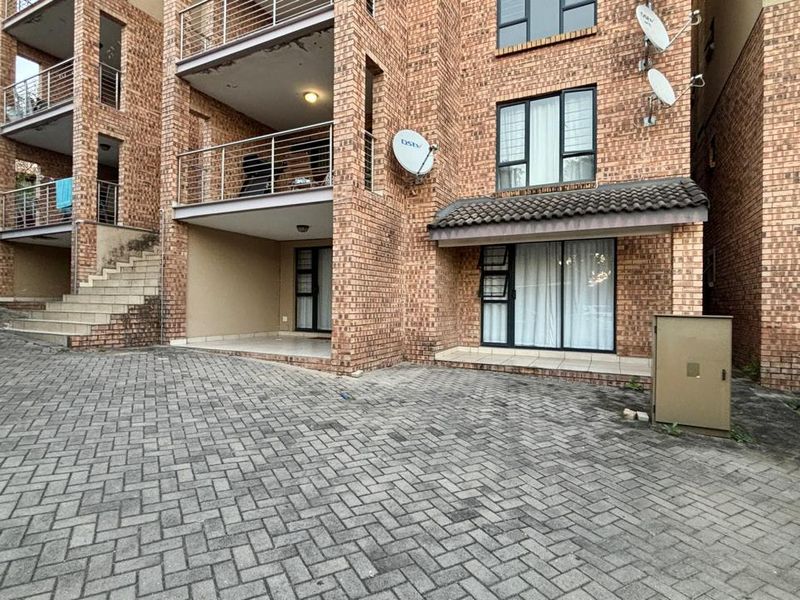Exterior view of a multi-story face brick apartment complex featuring paved driveway access, balconies, and aluminum window frames.
