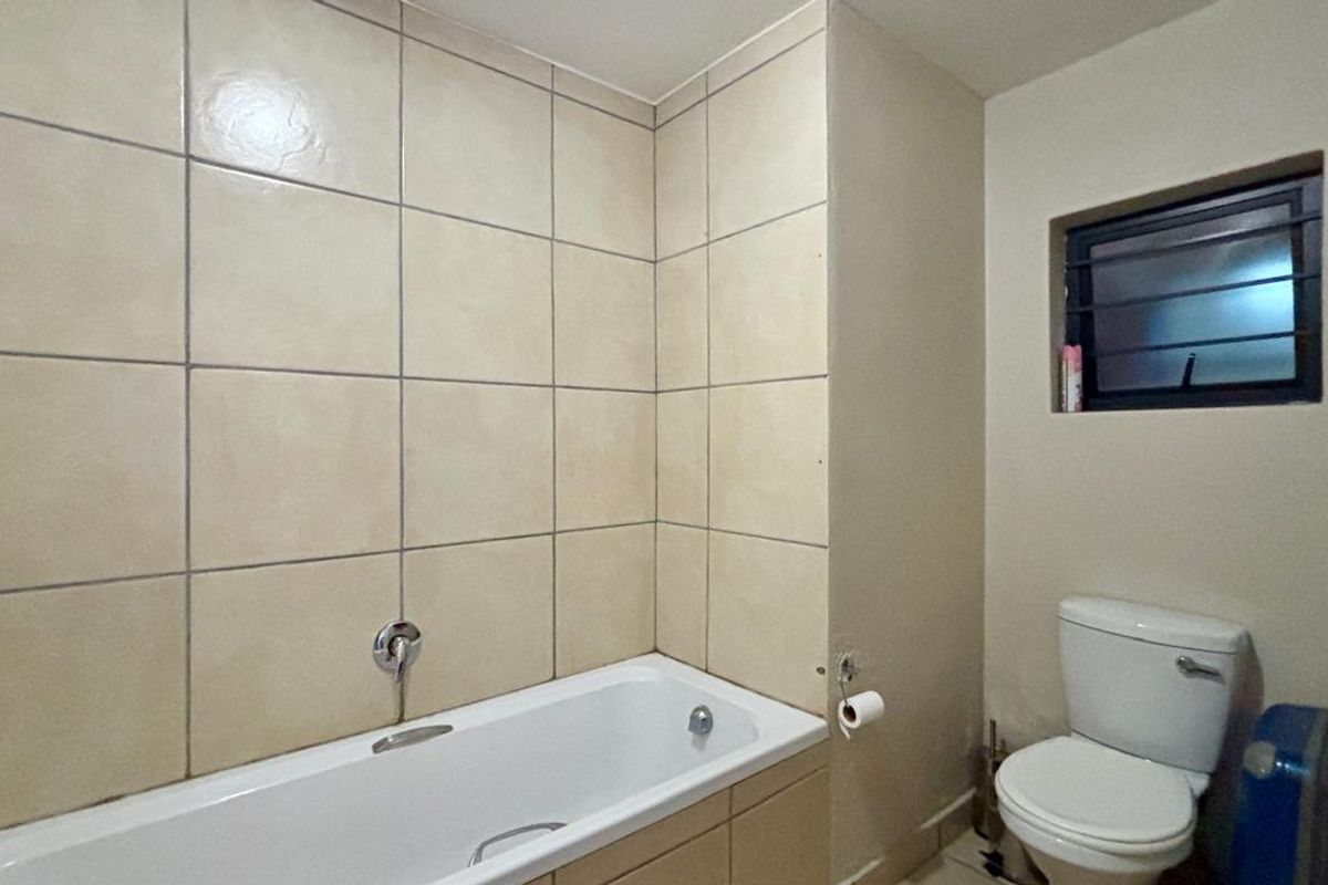 A functional bathroom featuring a bathtub with tiled surround and a standard toilet, complemented by a small window with security bars.
