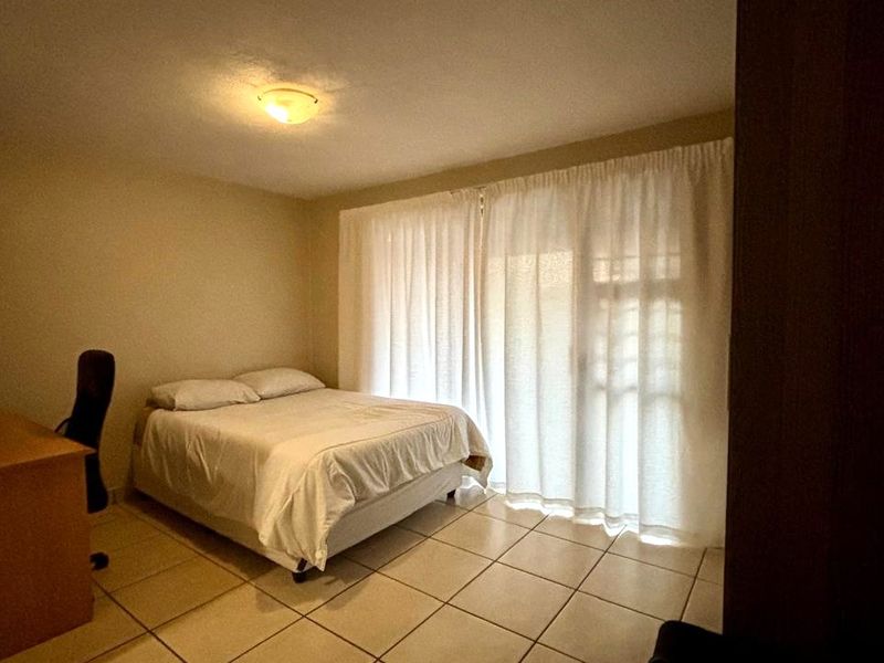 A bedroom featuring tiled flooring and a sliding glass door with curtains, providing access to an outdoor area.