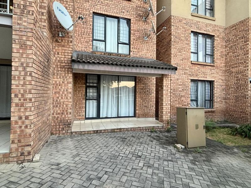 Exterior view of a face brick apartment building featuring a paved entrance area, tiled patio, and secure window fittings.