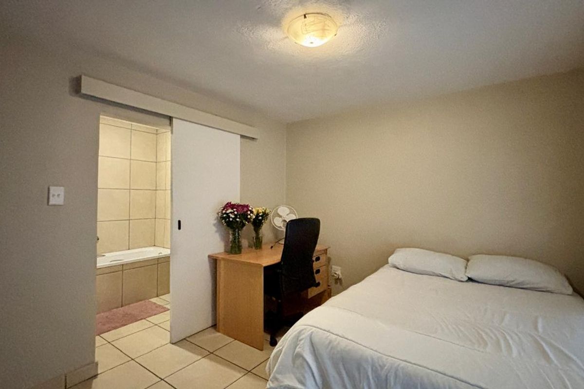 A bedroom featuring tiled flooring, a sliding door leading to an en-suite bathroom, and a central flush mount ceiling light.