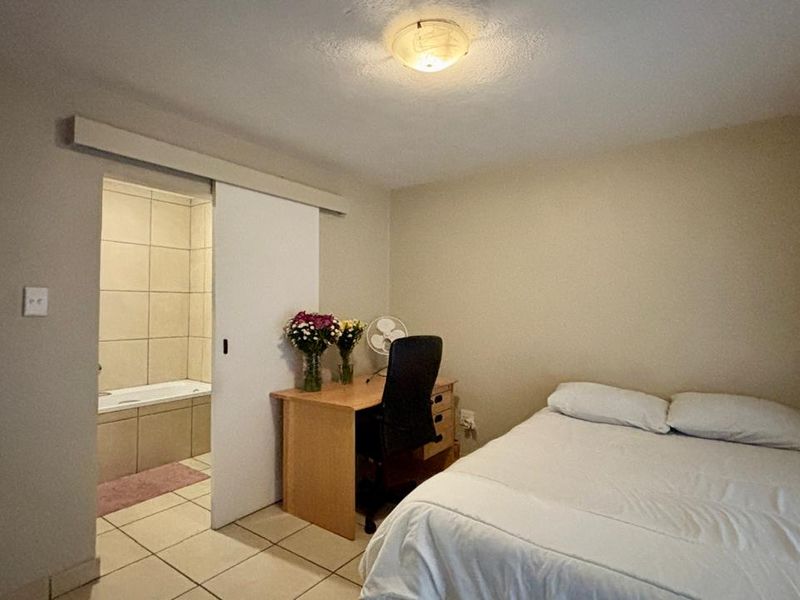 A bedroom featuring tiled flooring, a sliding door leading to an en-suite bathroom, and a central flush mount ceiling light.