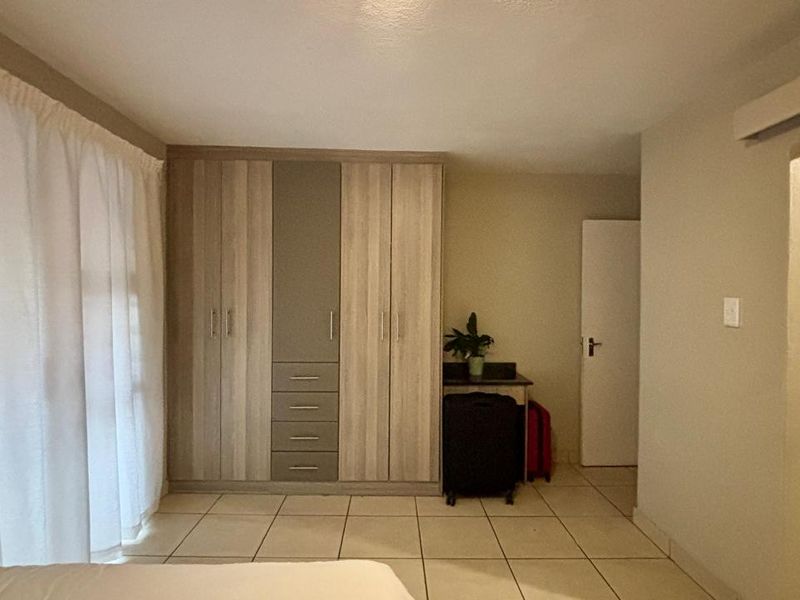 A well-maintained bedroom featuring built-in cupboards, neutral tiled flooring, and direct access to an en-suite bathroom.