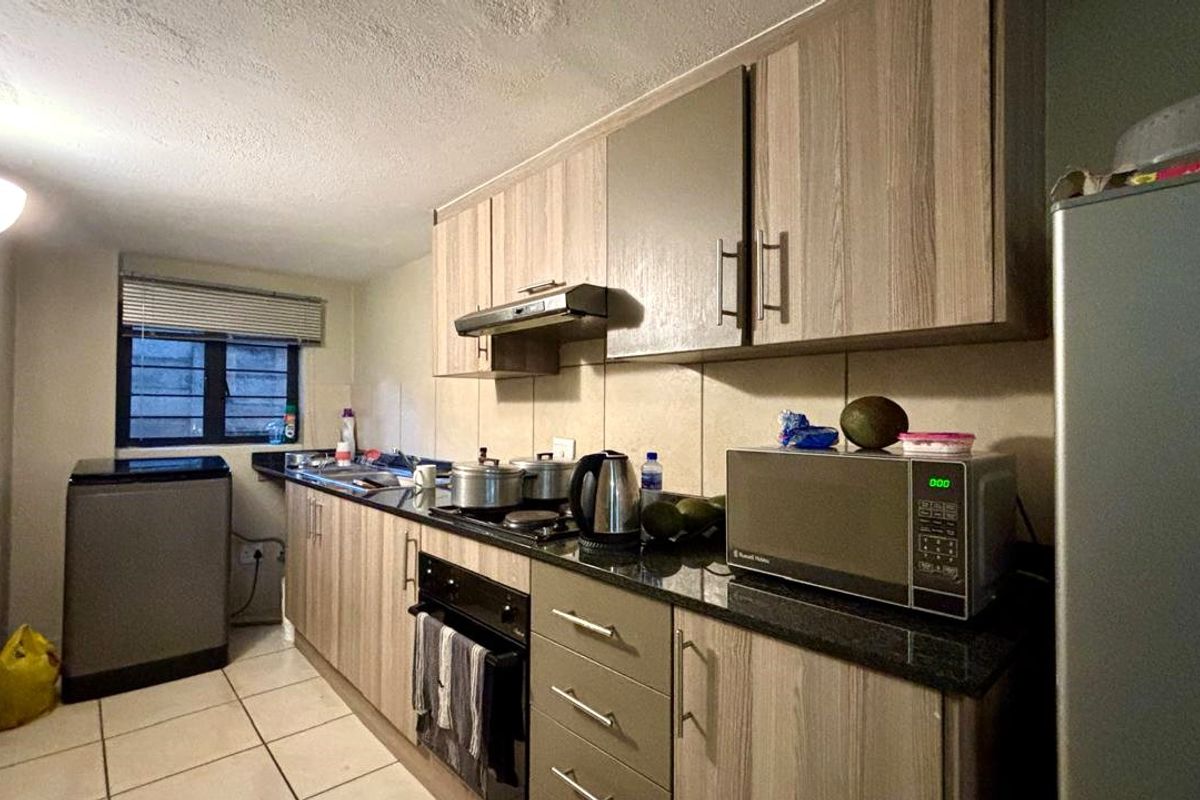 A functional kitchen featuring laminate cabinetry, granite countertops, built-in oven, hob, and extractor fan, with tiled flooring and backsplash.