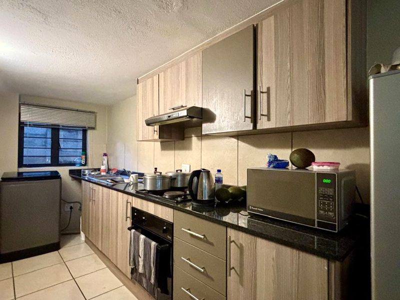 A functional kitchen featuring laminate cabinetry, granite countertops, built-in oven, hob, and extractor fan, with tiled flooring and backsplash.