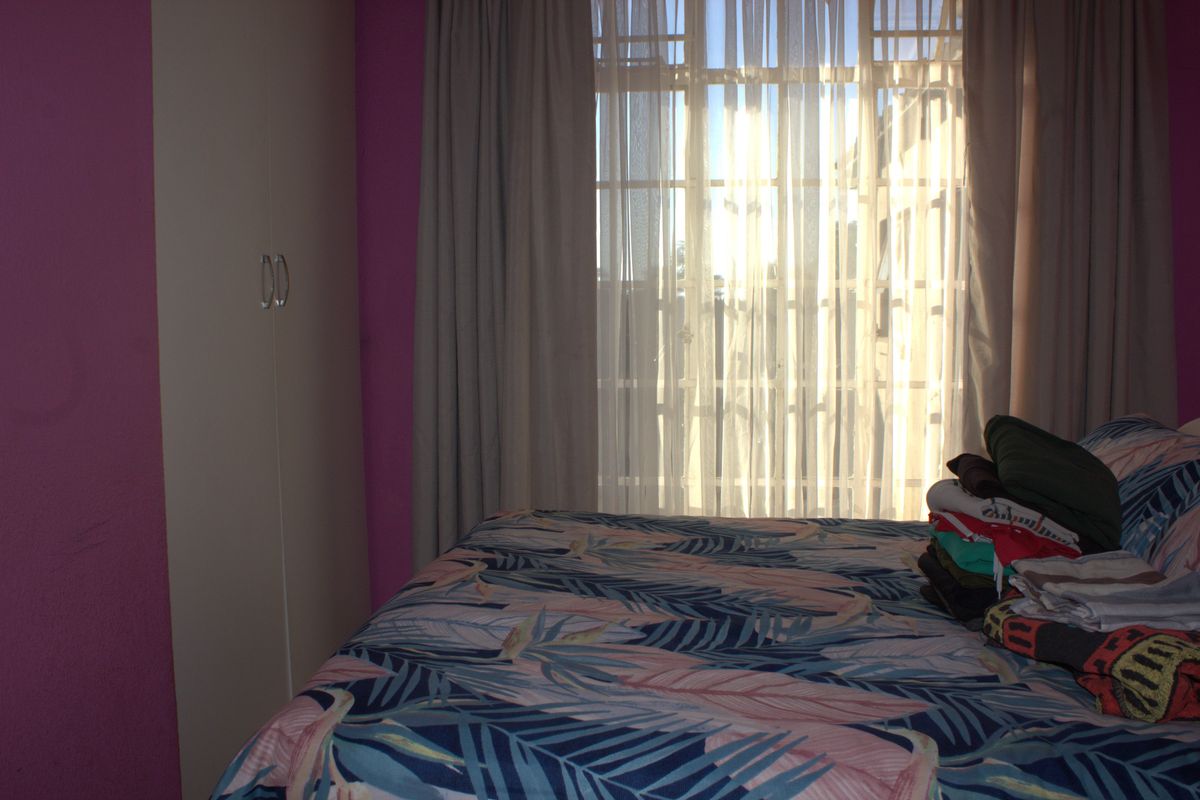A bedroom featuring built-in cupboards and large windows with curtains, allowing for natural light.