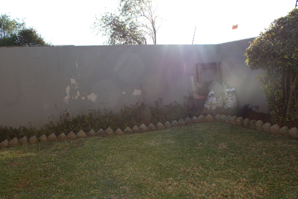 A private rear garden area featuring a lawn, established tree, and a boundary wall requiring maintenance.